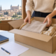 Manos colocando una prenda en una caja de cartón para su devolución, junto a una hoja y un cuaderno.