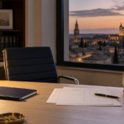 Escritorio al atardecer con hojas de registro horario, un cuaderno y un reloj, con Toledo al fondo.