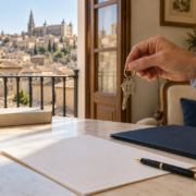 Mano sosteniendo unas llaves sobre una mesa con documentos en una vivienda con vistas a Toledo.