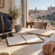 Bolsa de viaje y agenda sobre una mesa junto al brazo vendado de una persona, con Toledo al fondo.